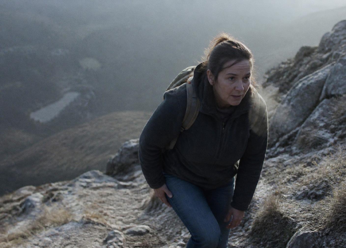 A hiker climbing a steep rocky trail through cold morning mist